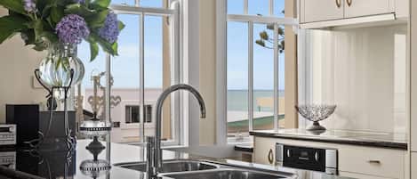 A modern kitchen with a large island, stainless steel appliances, and a view of the sea.