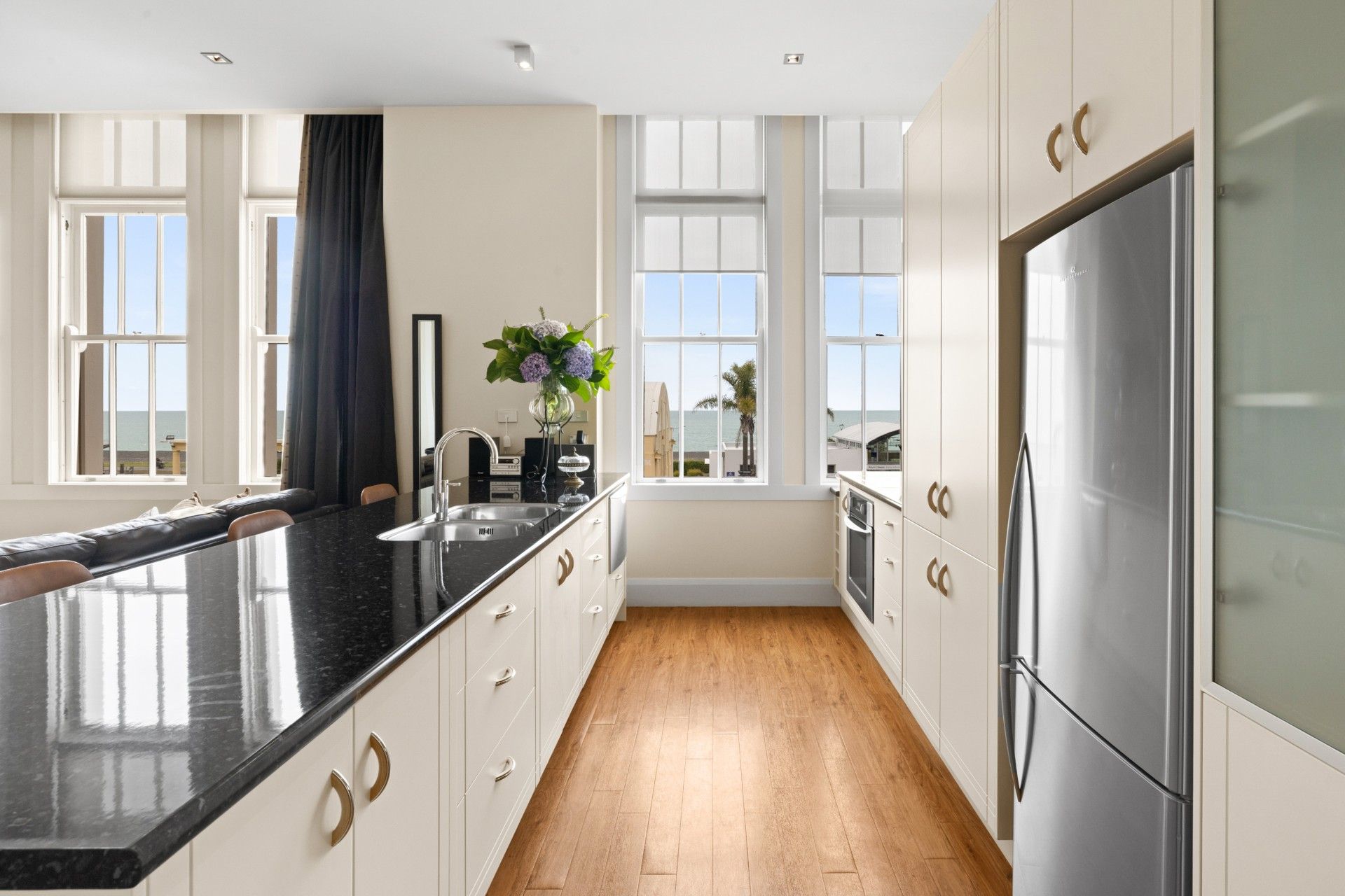 A modern kitchen with a black countertop, stainless steel appliances, and large windows offering a view of the outdoors.