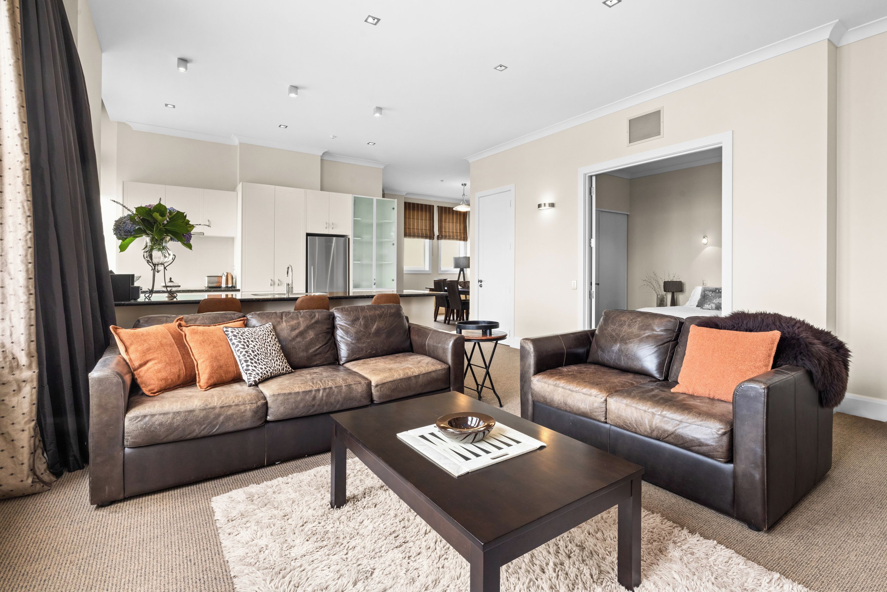 A modern living room with a sectional sofa, a coffee table, and a dining area in the background.