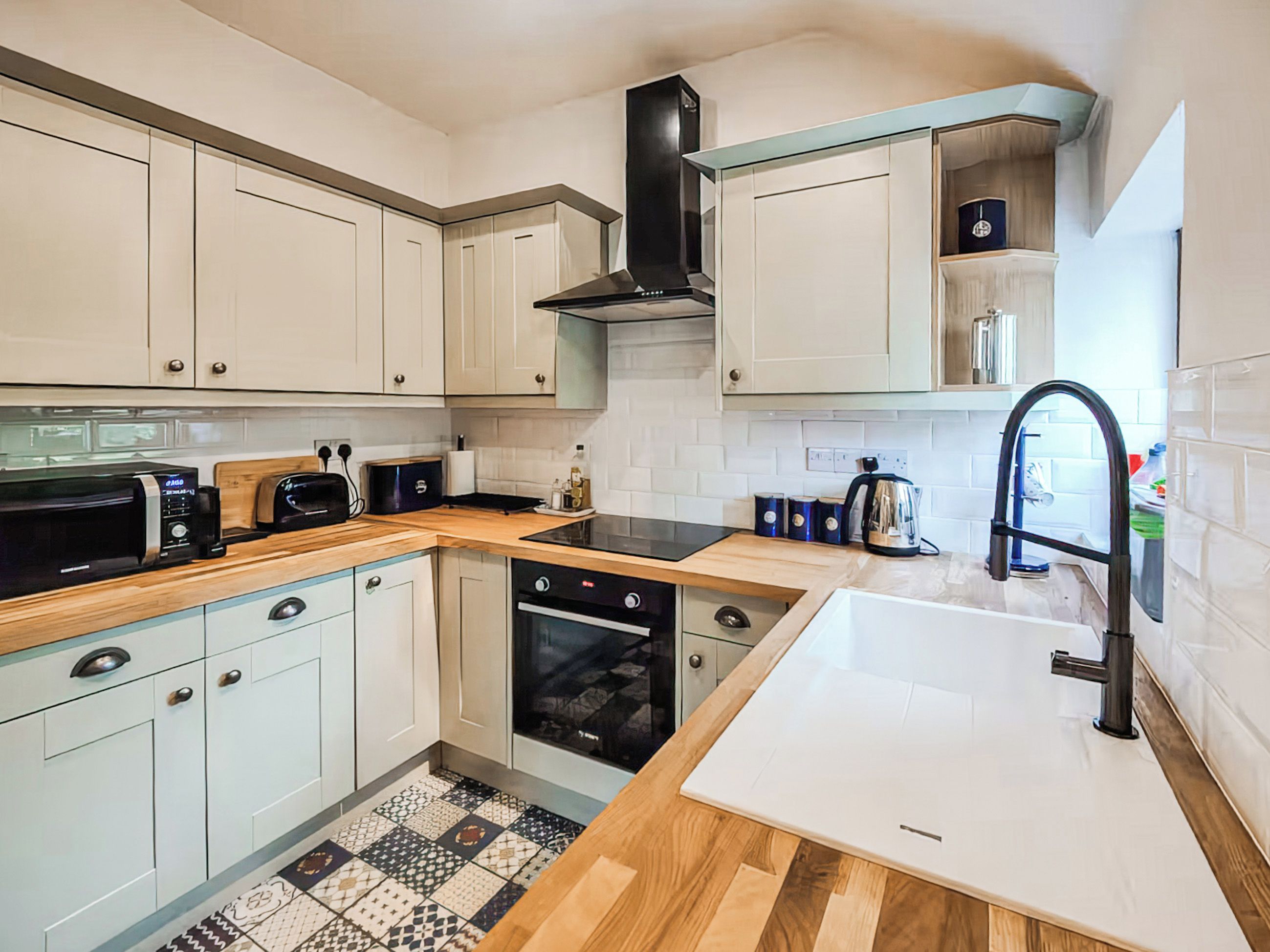 A modern kitchen with white cabinetry, a black range hood, a built-in oven, and a wooden countertop.