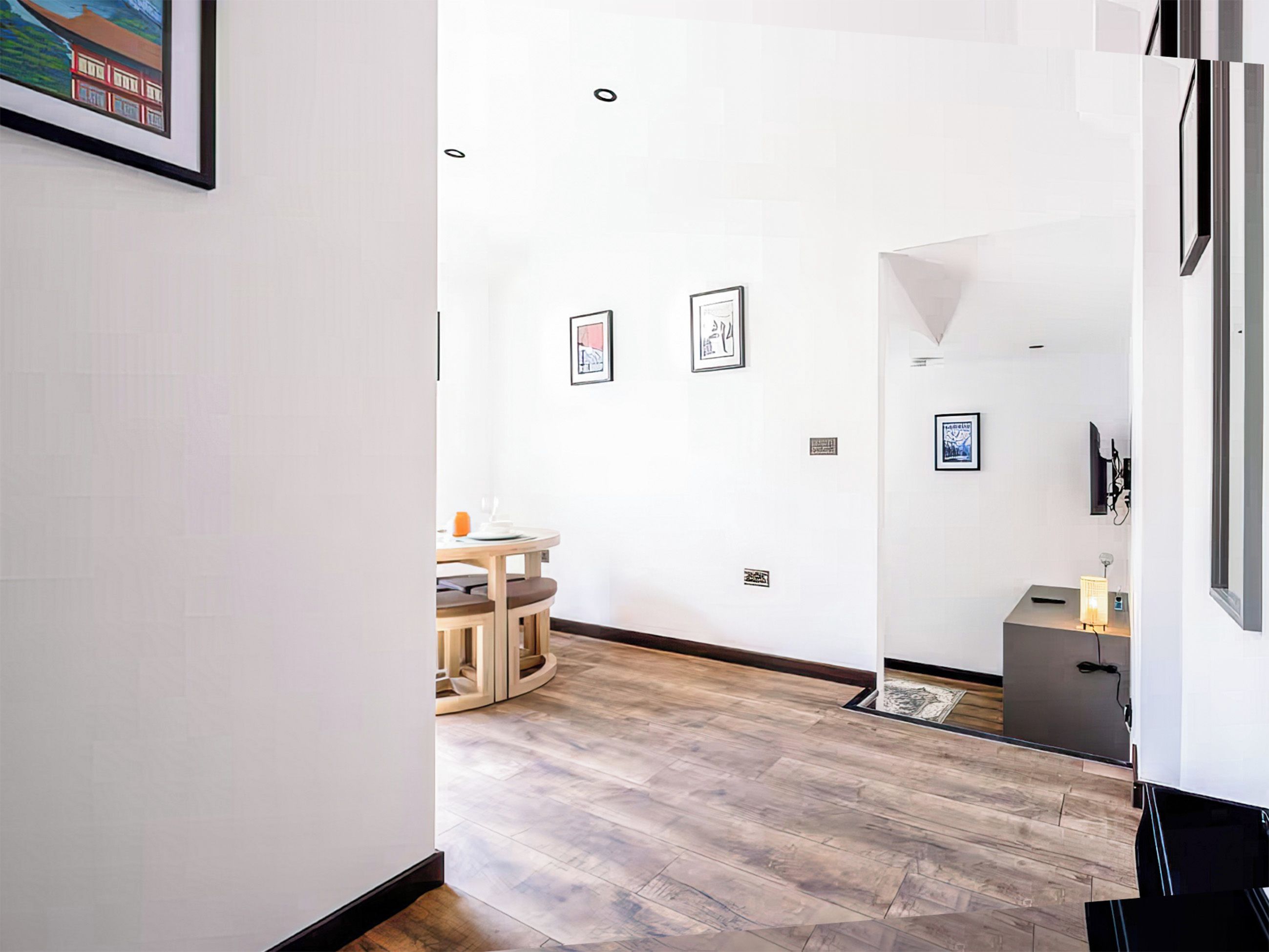 A modern interior with a dining area, framed artwork on the walls, and a wooden floor.