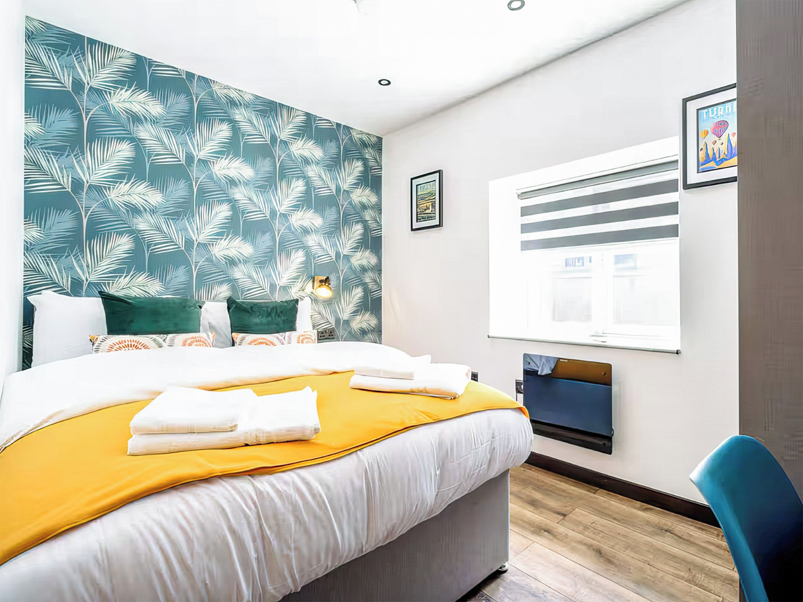 A hotel room with a bed, a window with blinds, a desk, and a chair.