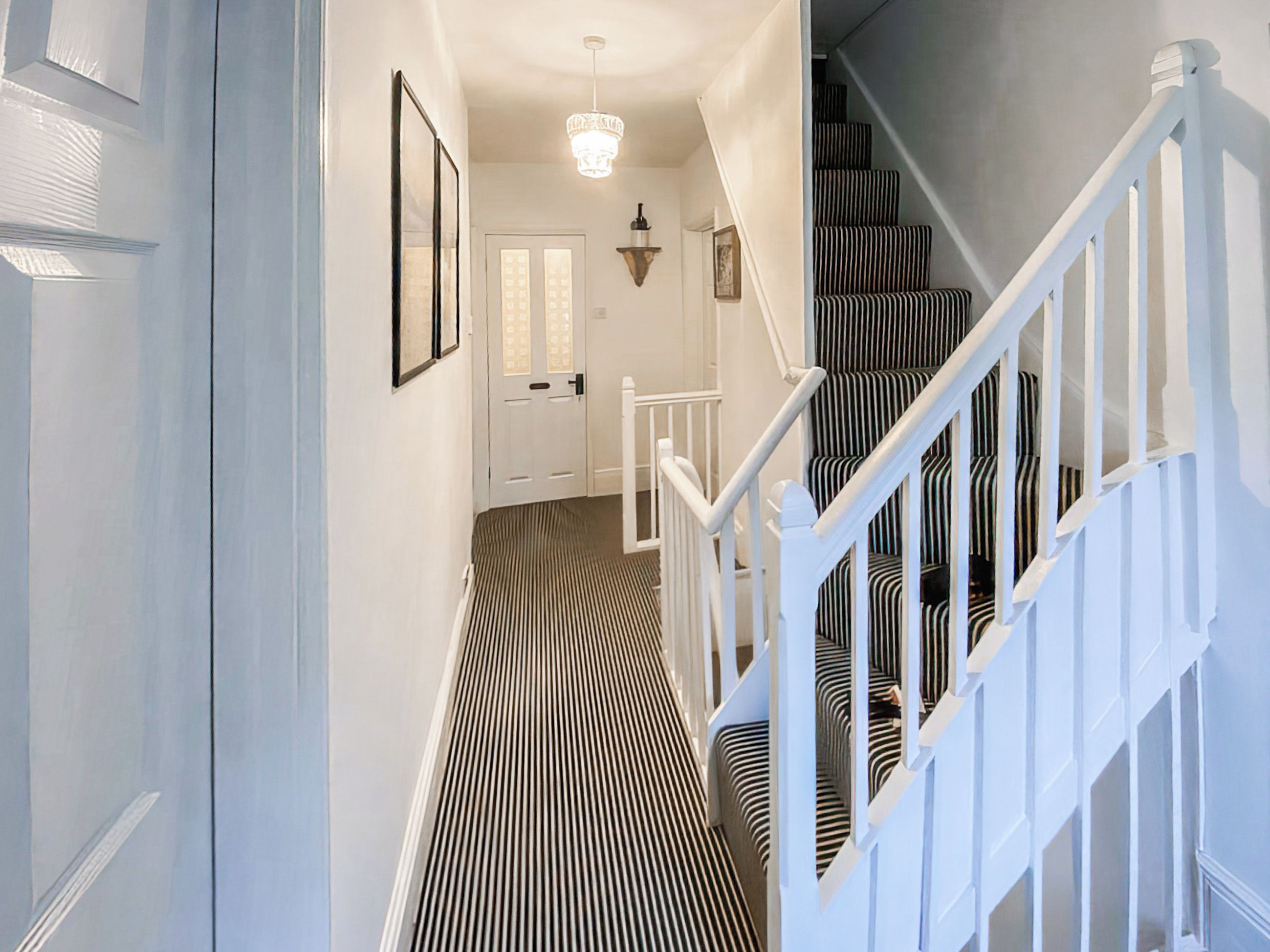 A hallway with a striped floor leading to a staircase with white railings.