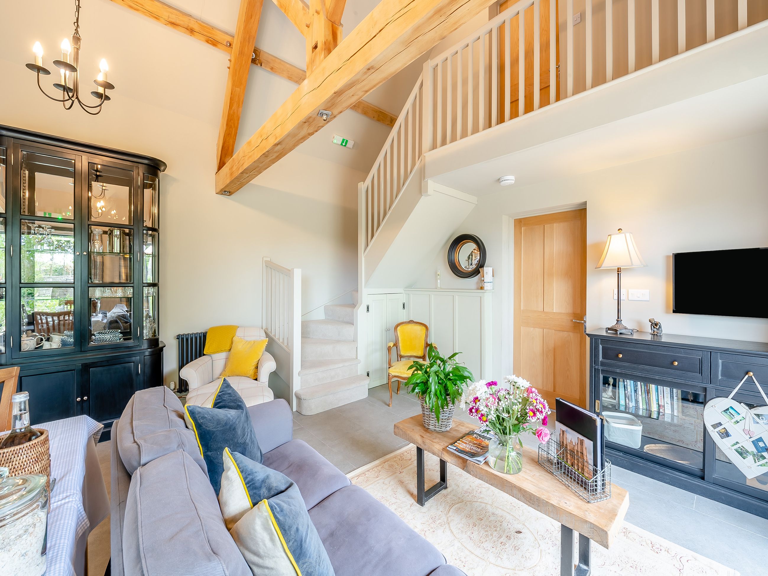 A spacious living area with a high ceiling, a staircase, a dining area, and a television mounted on the wall.