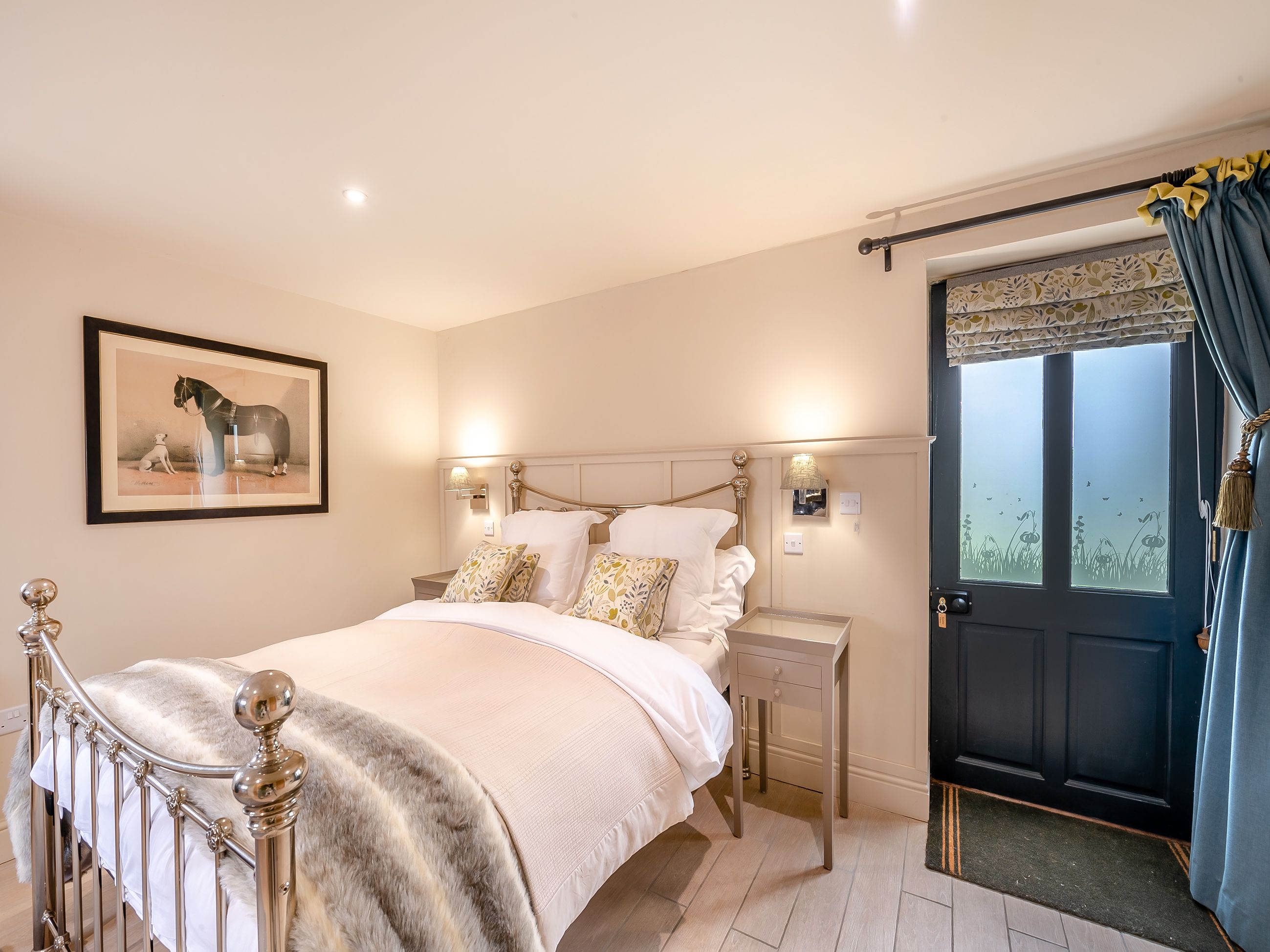 A bedroom with a bed, bedside tables, a framed picture, and a door with a view.