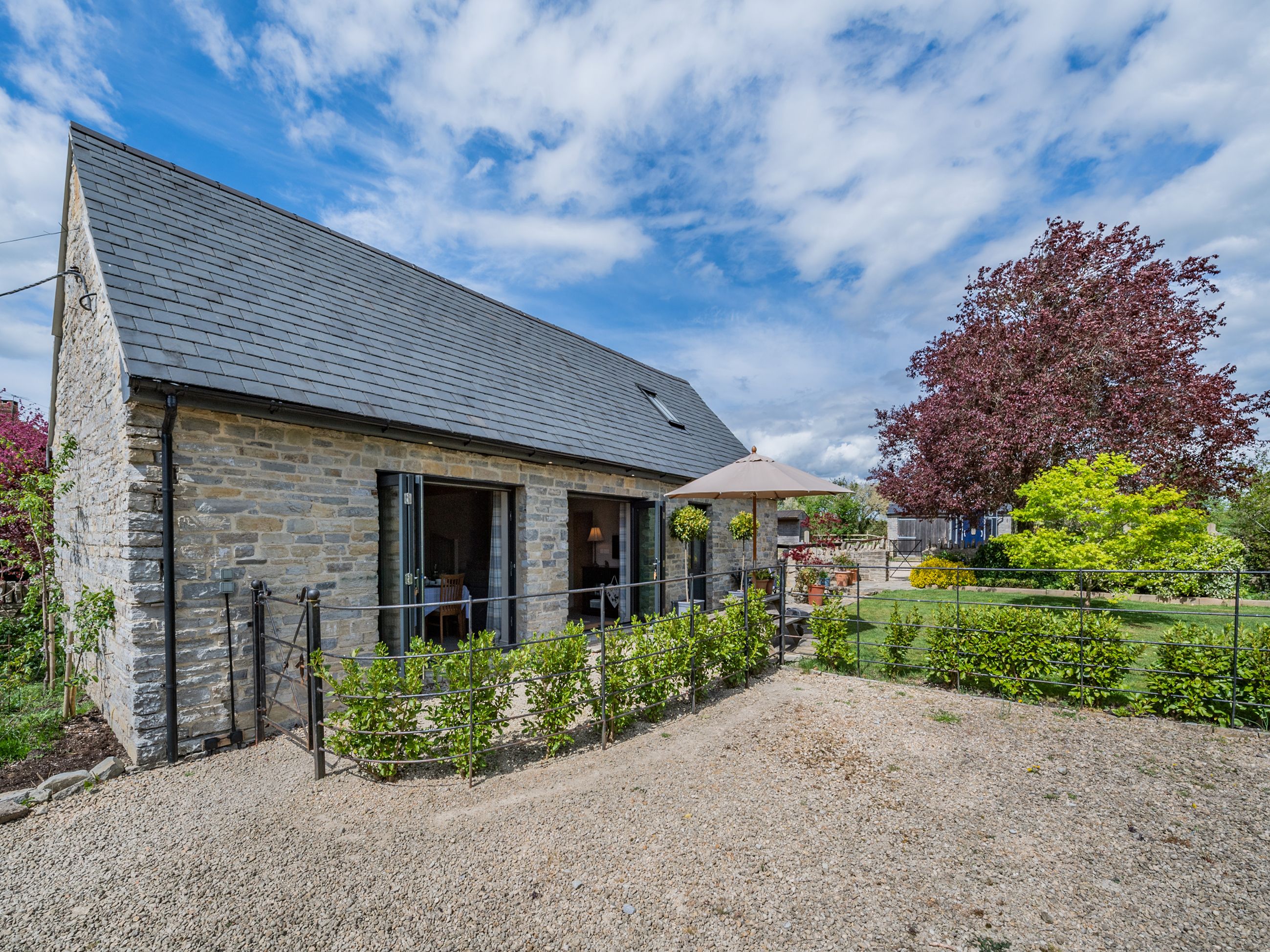 A stone building with a gravel driveway and a fenced garden area.