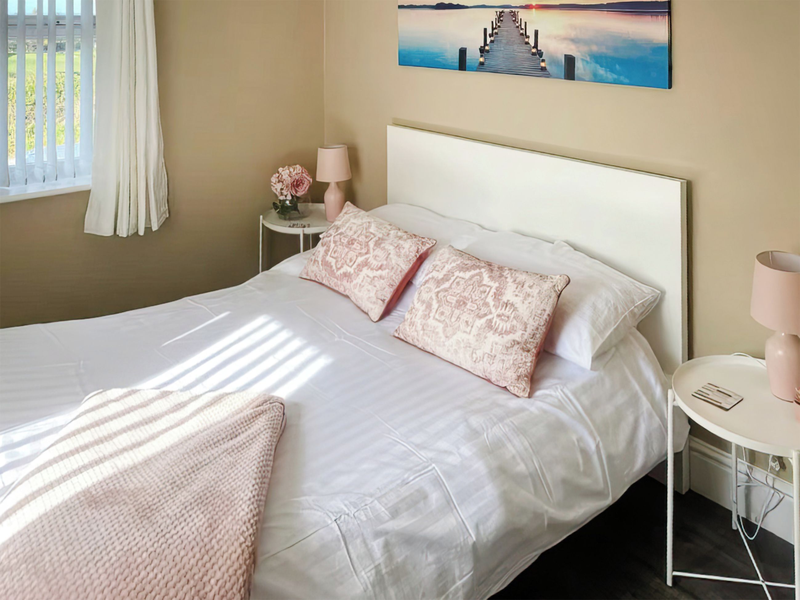 A neatly made bed with patterned pillows, a bedside table with a lamp, and a painting of a sunset on the wall.