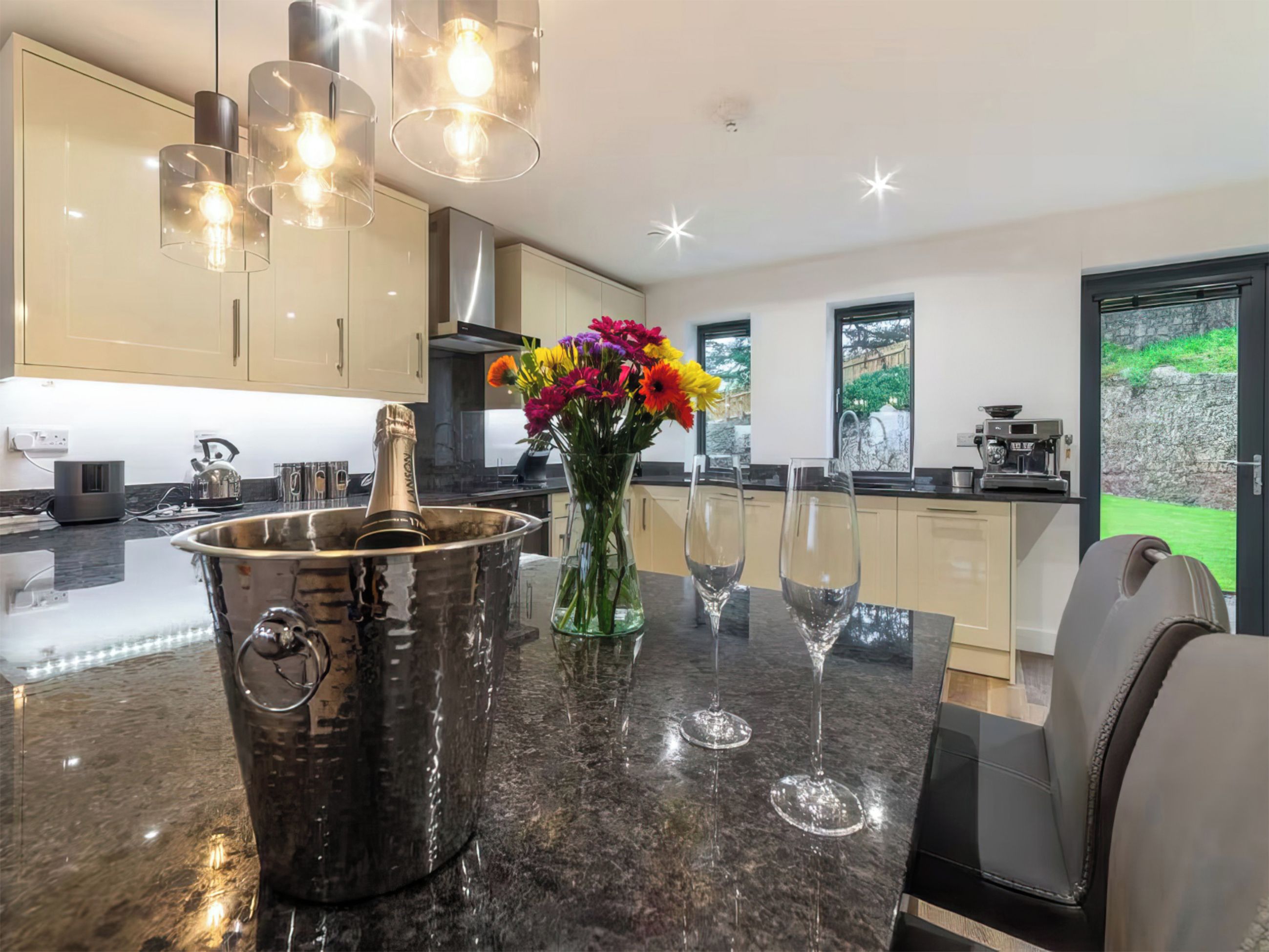 A modern kitchen with a marble countertop, a champagne bucket, wine glasses, and a vase of flowers.