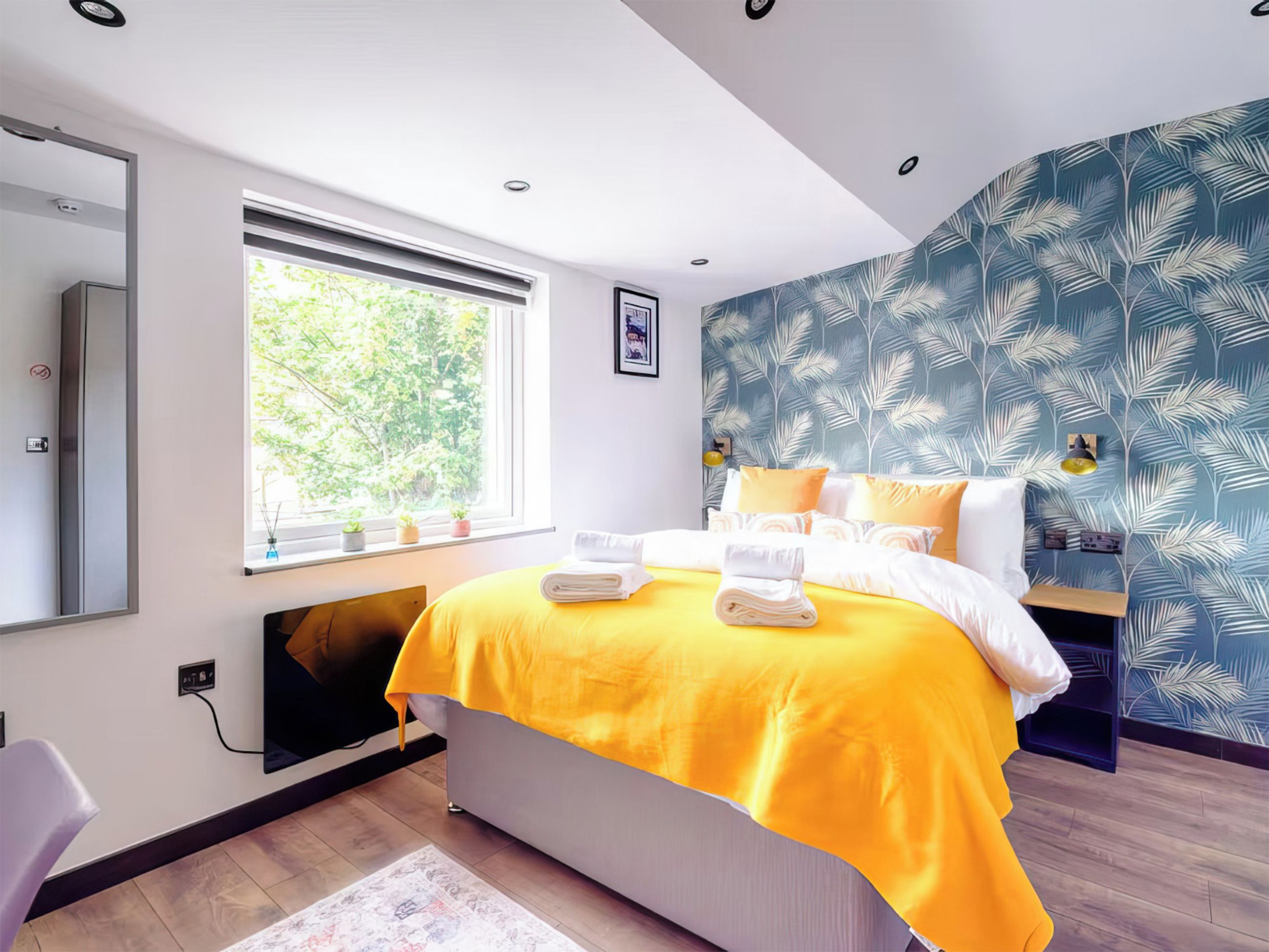 Ein modernes Schlafzimmer mit einem Bett, einem Fenster, einem Spiegel und einer Wand mit einem Blattmuster.