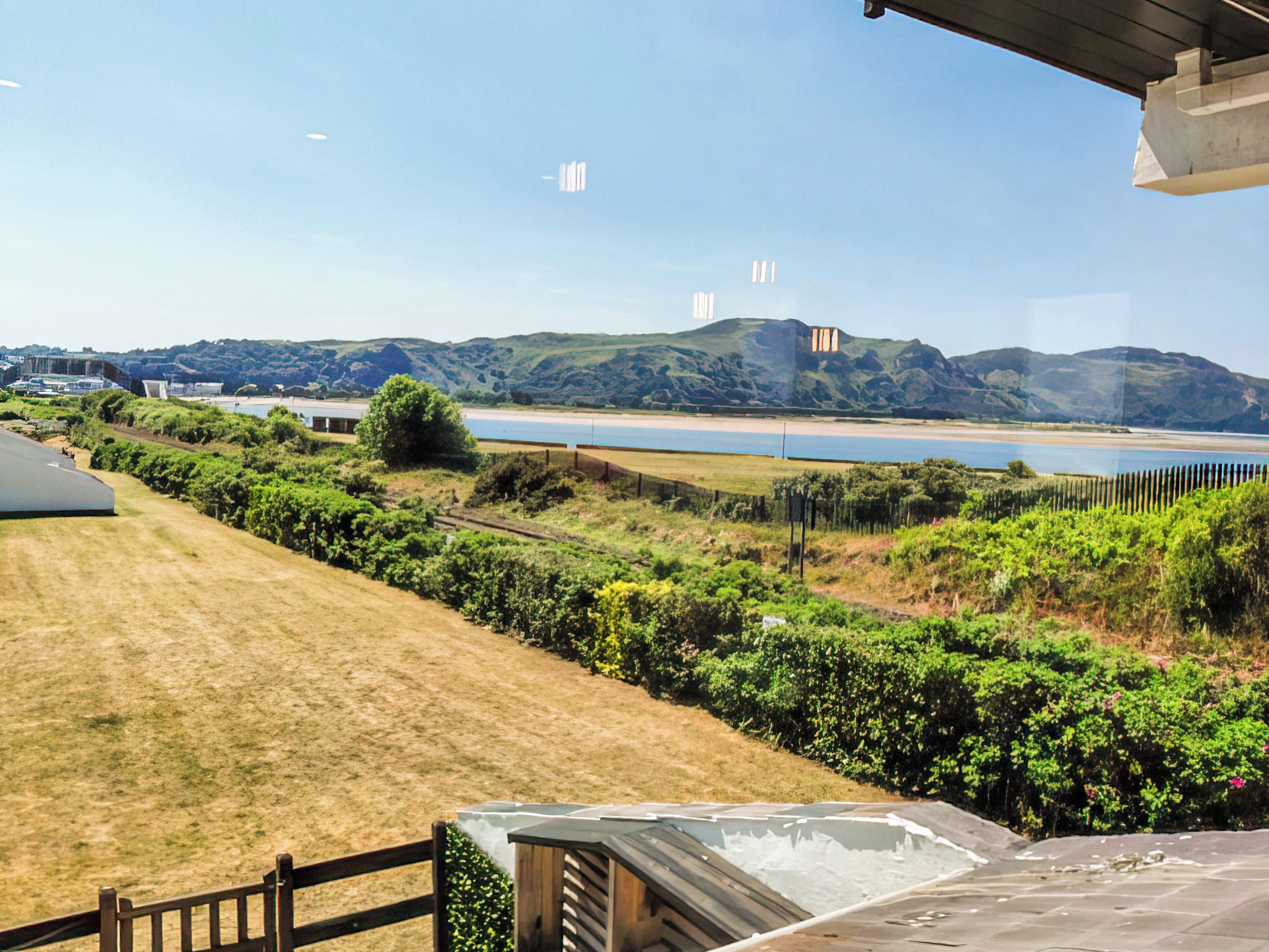 A view of a coastal landscape with a grassy area, a body of water, and hills in the distance.