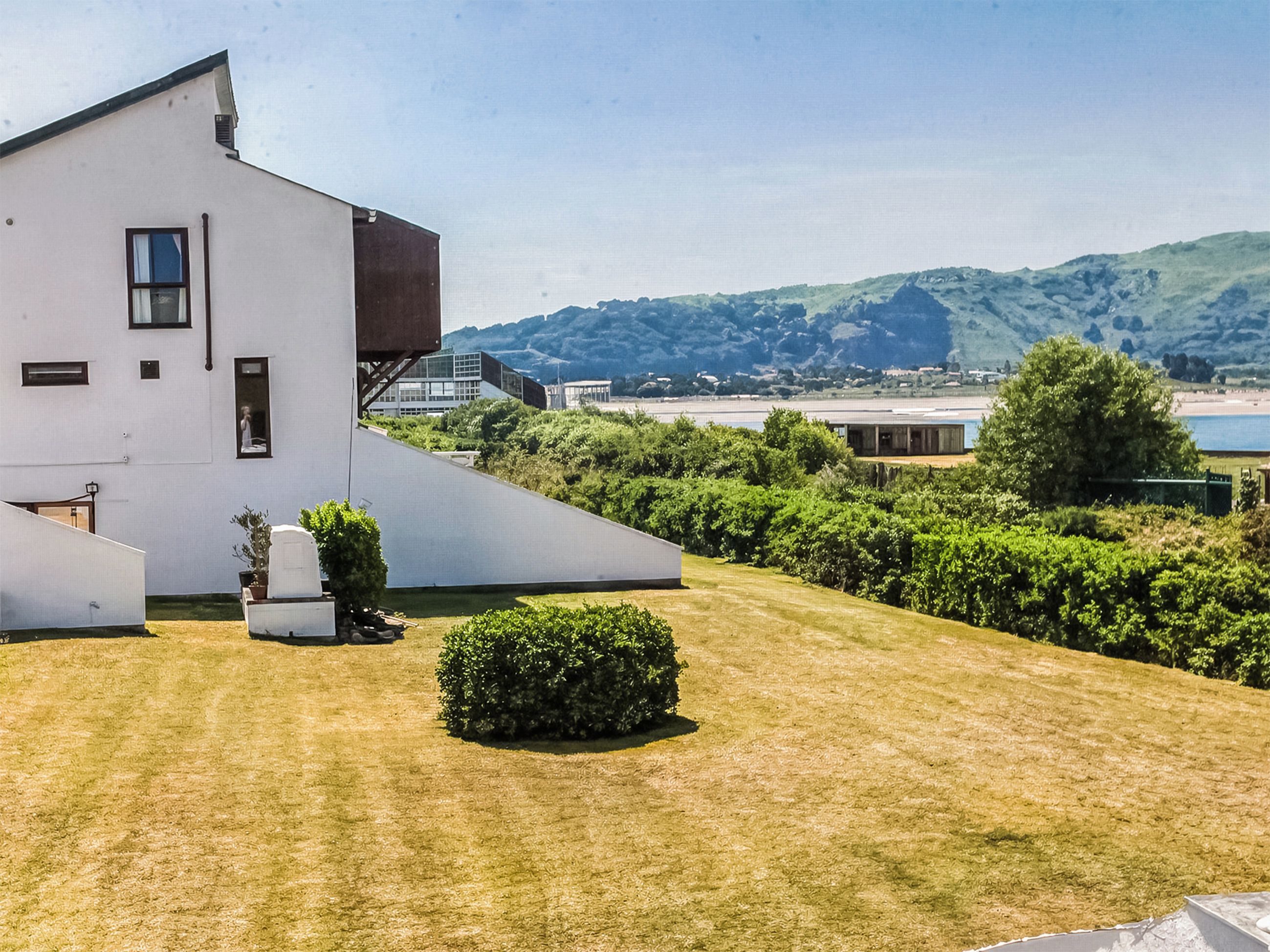 Un bâtiment moderne doté d’un toit en pente, d’un petit jardin agrémenté d’une haie, et offrant une vue sur un paysage vallonné en arrière-plan.