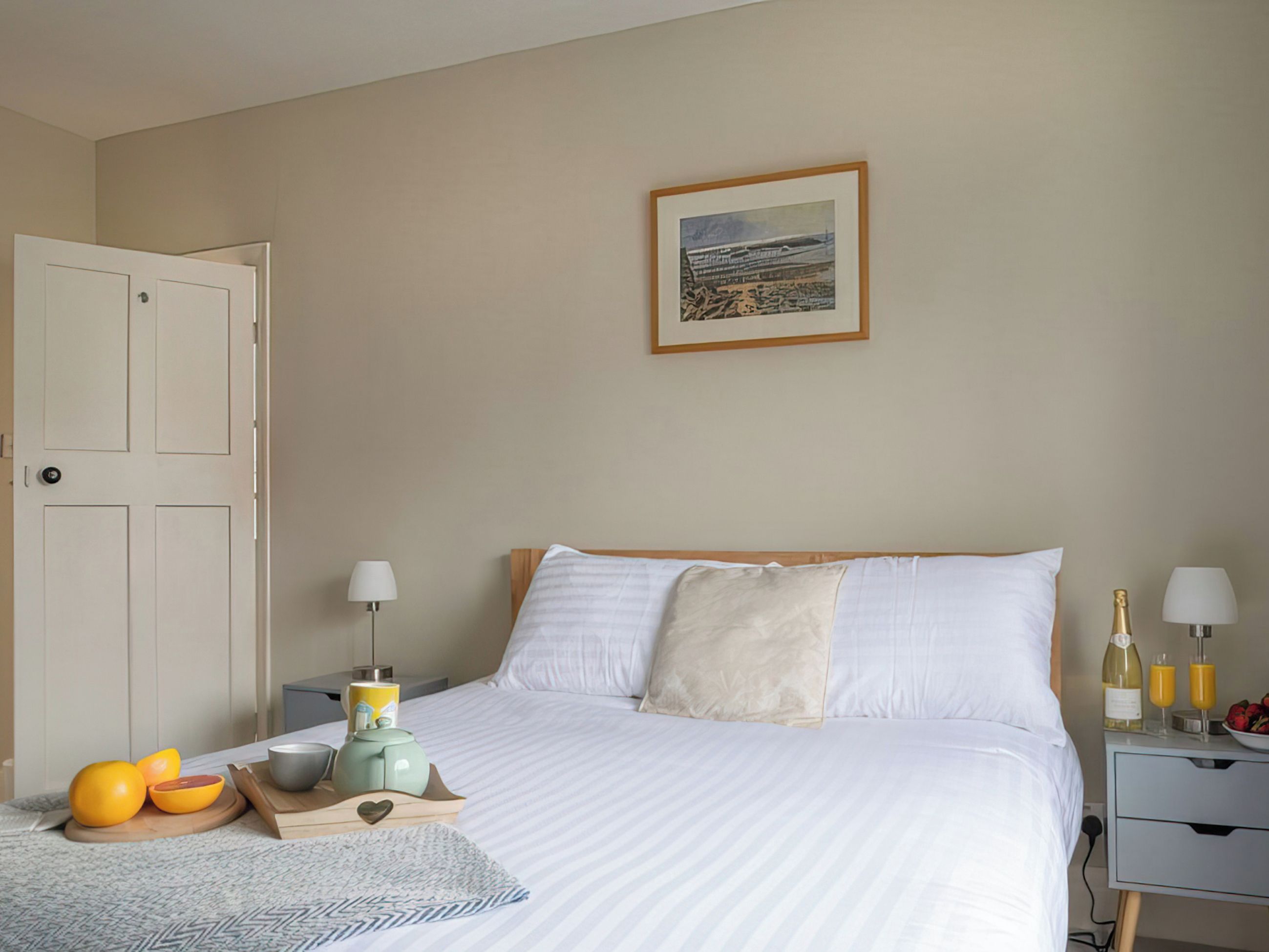 Habitación de hotel ordenada con cama, mesitas de noche, un cuadro en la pared y una puerta.