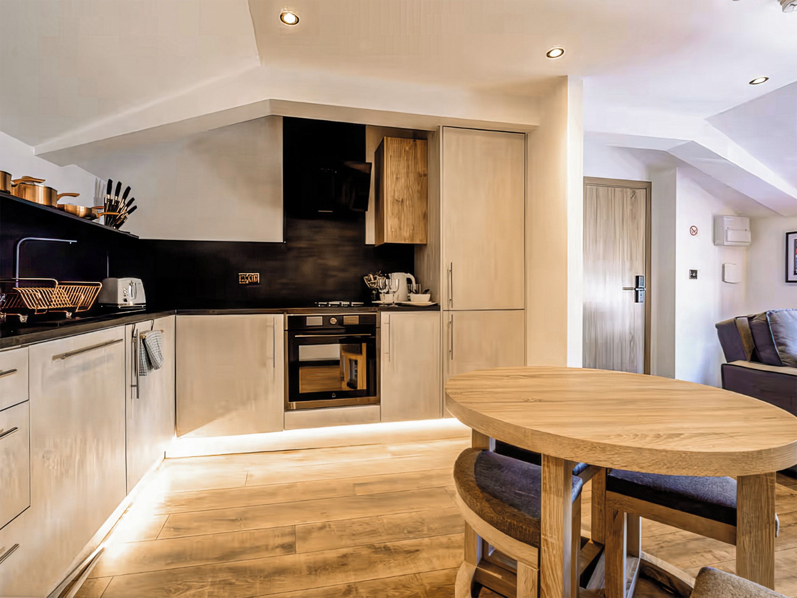 A modern kitchen with wooden cabinets, a built-in oven, and a dining area with a round table and chairs.