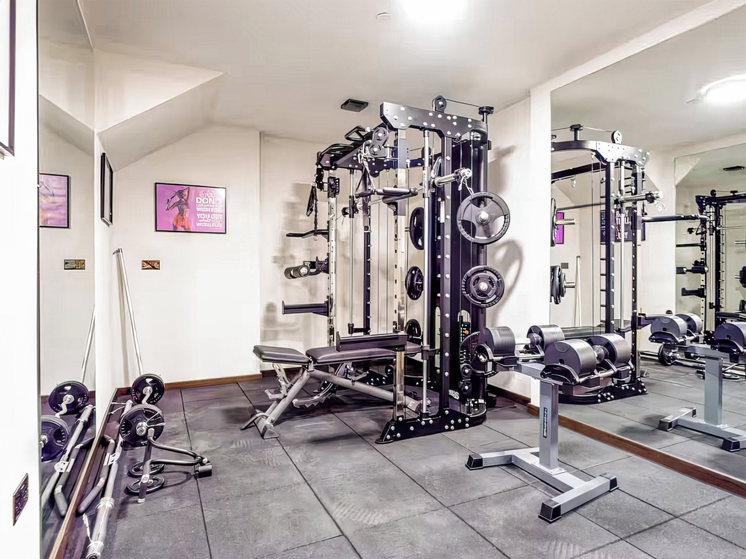 Ein Fitnessraum mit verschiedenen Gewichteinrichtungen, einer Hantelbank und einem Spiegel an der Wand.