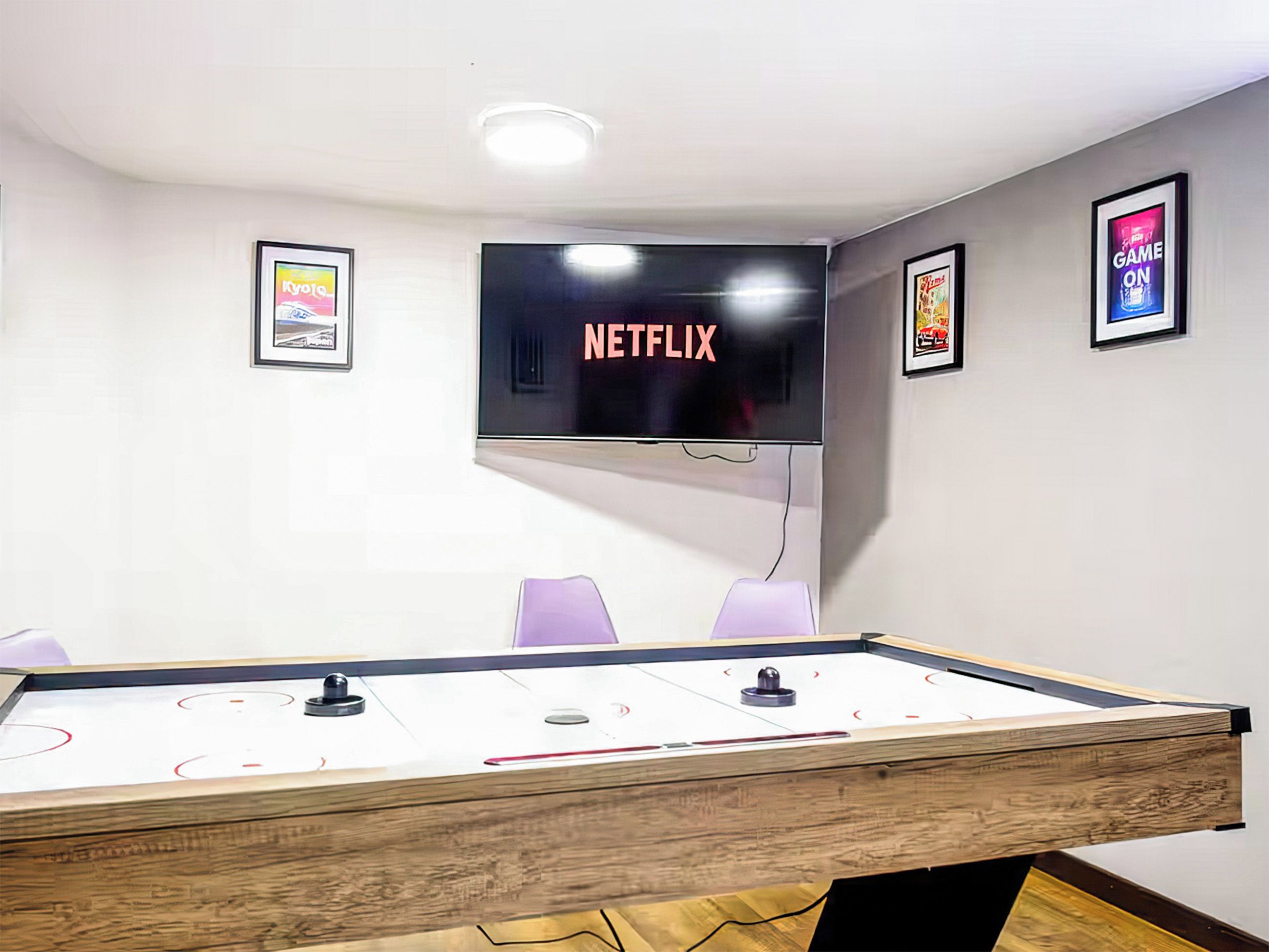 Quarto com mesa de bilhar, televisão fixada exibindo 'NETFLIX' e pôsteres emoldurados nas paredes.