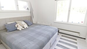 Ein Schlafzimmer mit einem Bett, Kissen, Kuscheltieren, einer Heizung und einem Fenster.