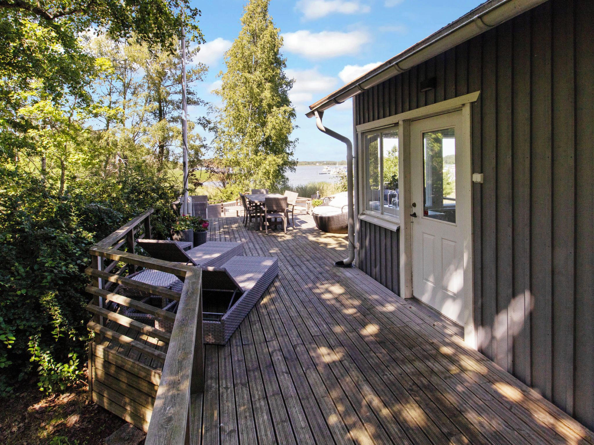 A wooden deck with outdoor furniture, a view of the water, and a building with a door and windows.