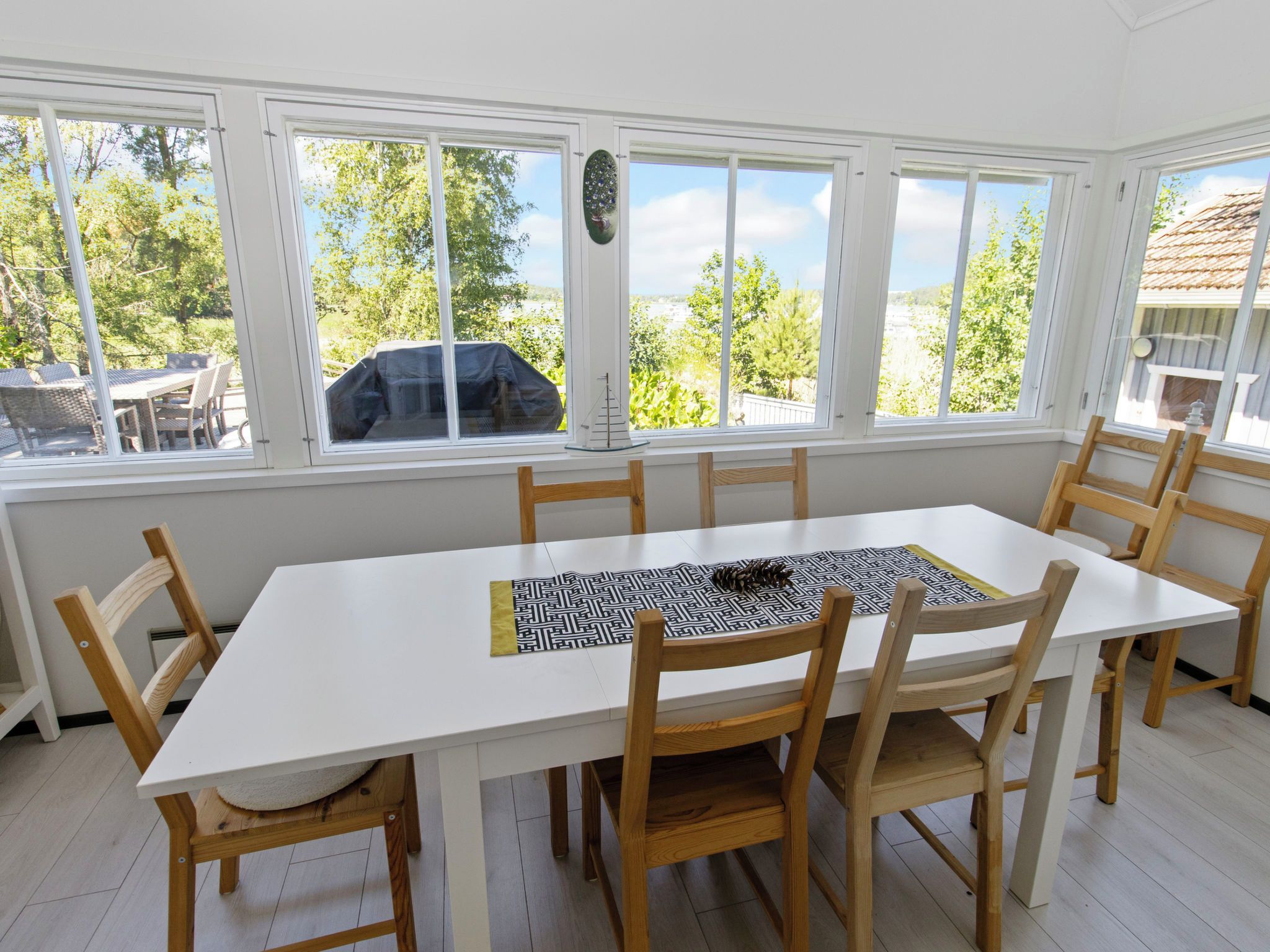 A dining area with a white table and wooden chairs, large windows with a view of trees and a building, and a decorative item on the windowsill.