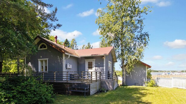Ein zweistöckiges Haus mit Veranda, einer kleinen Terrasse und Blick auf einen See mit Booten.