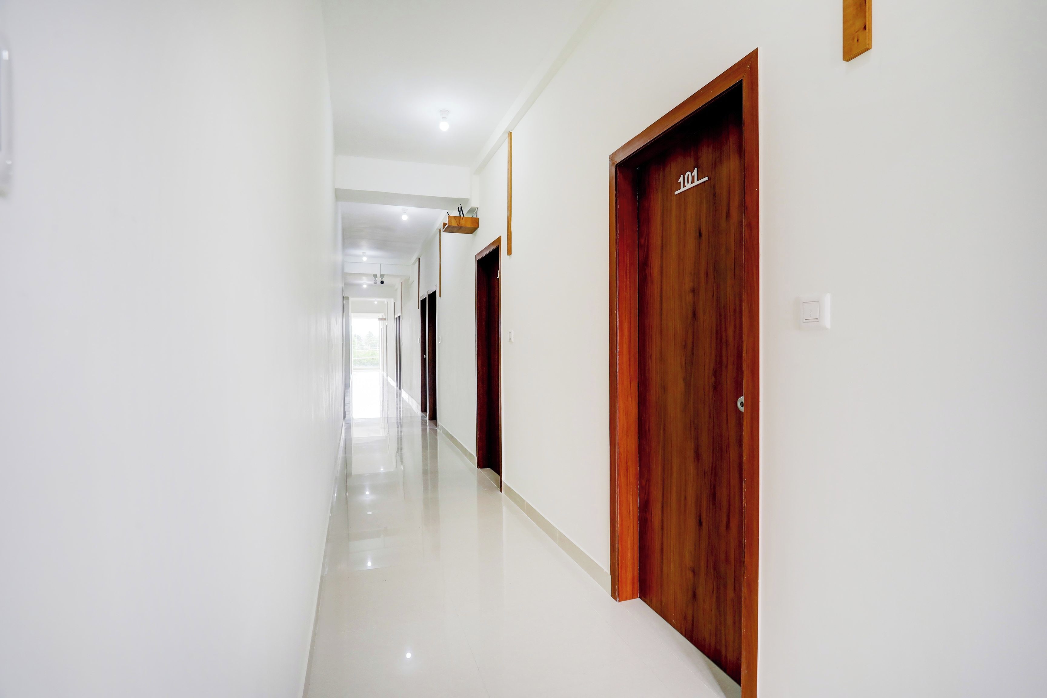 Un pasillo con paredes blancas y puertas de madera que conduce a una habitación luminosa.