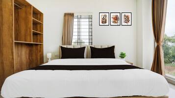 Une chambre d’hôtel avec un grand lit, une armoire en bois, une fenêtre avec des rideaux et trois œuvres d’art encadrées accrochées au mur.