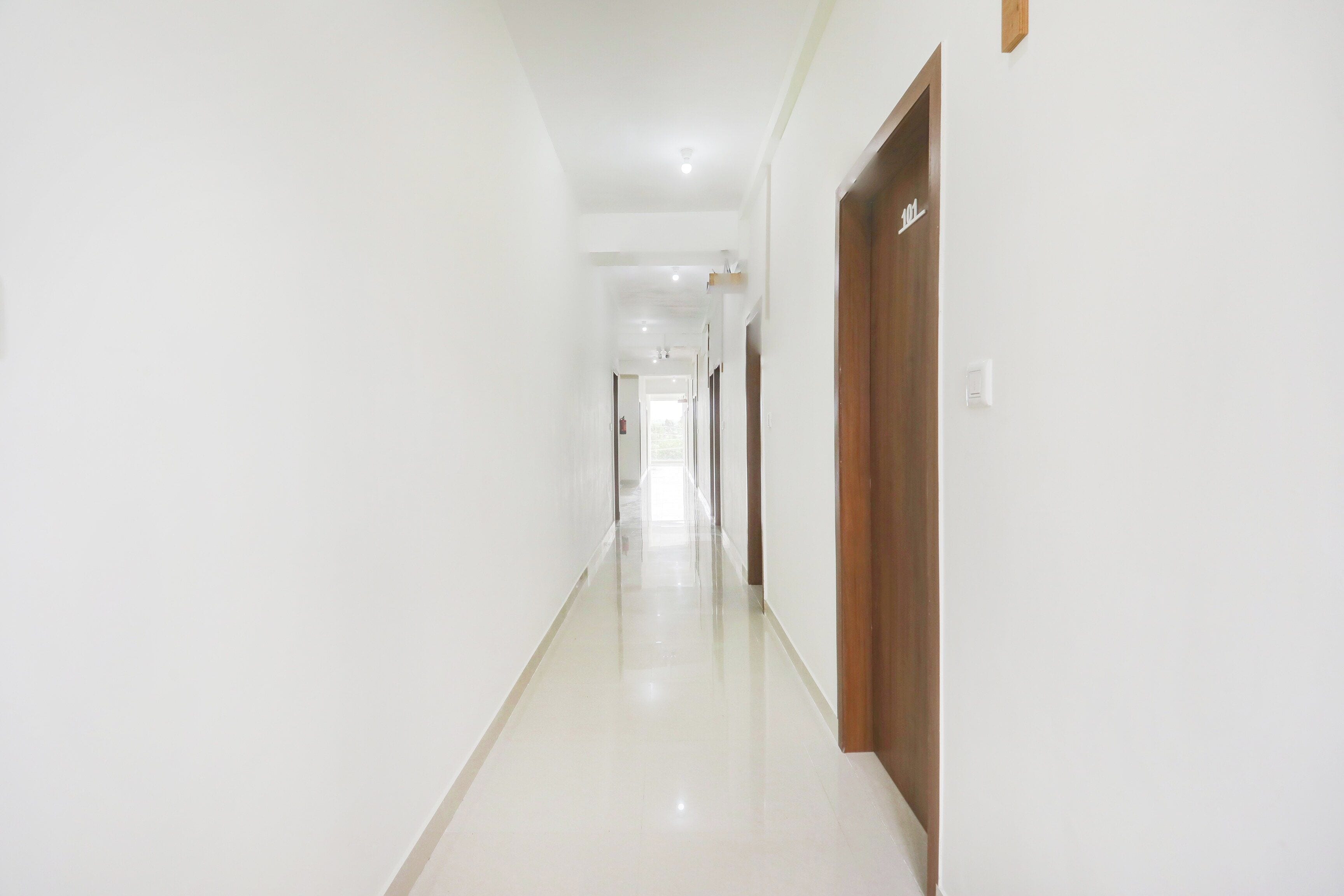 A long, narrow hallway with white walls and a shiny floor, leading to a door at the end.