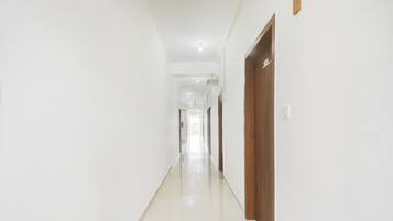 A long, narrow hallway with white walls and a shiny floor, leading to a door at the end.