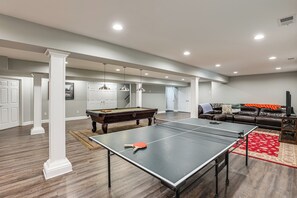 Amplia sala de estar con mesa de billar, mesa de ping pong y sofá de cuero.
