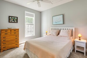Ein Schlafzimmer mit einem Bett, einem Schminktisch, einem Nachttisch, einer Lampe und zwei gerahmten Bildern an der Wand.