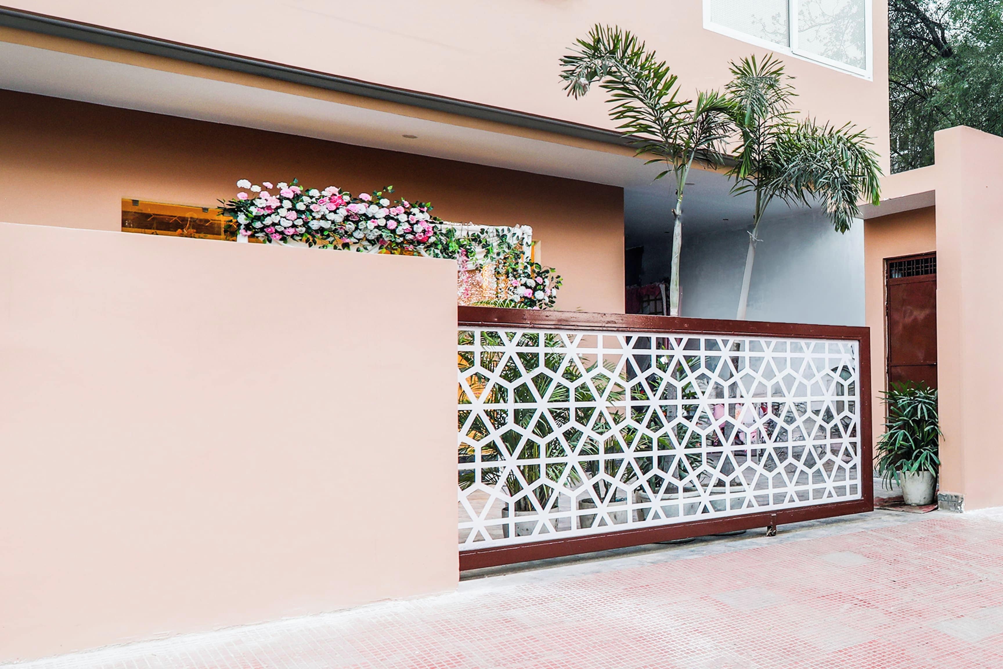 A modern building with a pink facade, a decorative white fence, and a small garden area with plants and flowers.