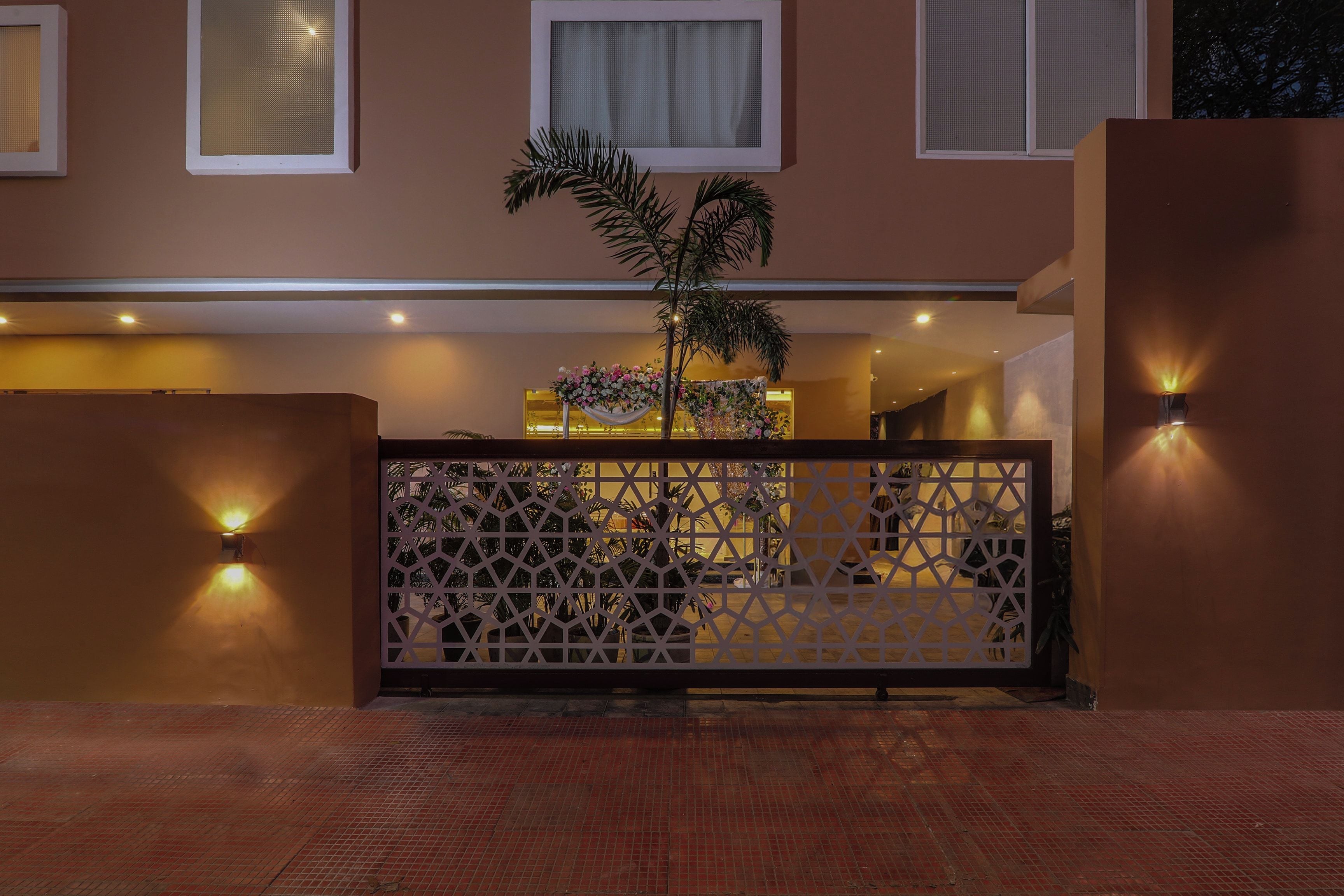 Entrada de un hotel con una puerta decorativa, una palmera y luces fijadas en la pared.
