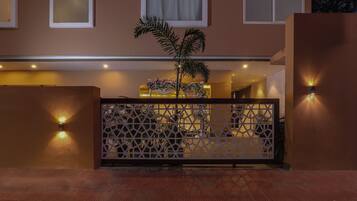Entrada de un hotel con una puerta decorativa, una palmera y luces fijadas en la pared.