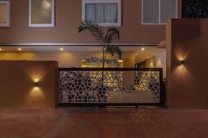A hotel entrance with a decorative gate, a palm tree, and wall-mounted lights.