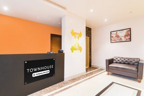 Un espace d’accueil avec une enseigne indiquant « TOWNHOUSE, entreprise de services », un comptoir d’accueil, un canapé et un mur orné d’un motif géométrique.