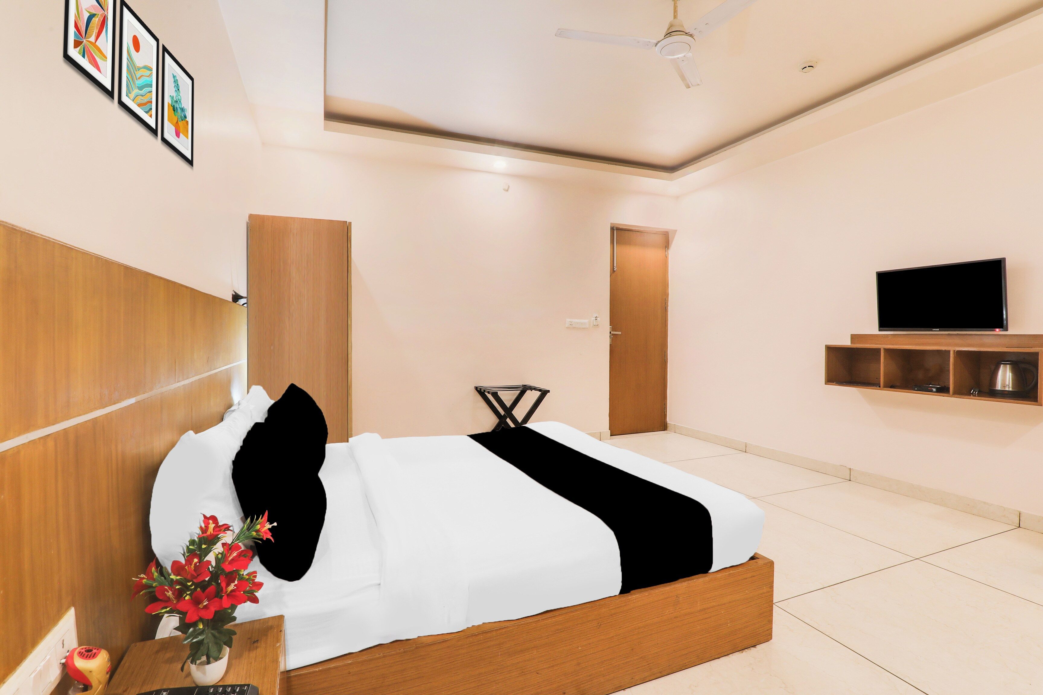 A hotel room with a bed, a TV, a wooden headboard, a wall-mounted shelf, and a ceiling fan.