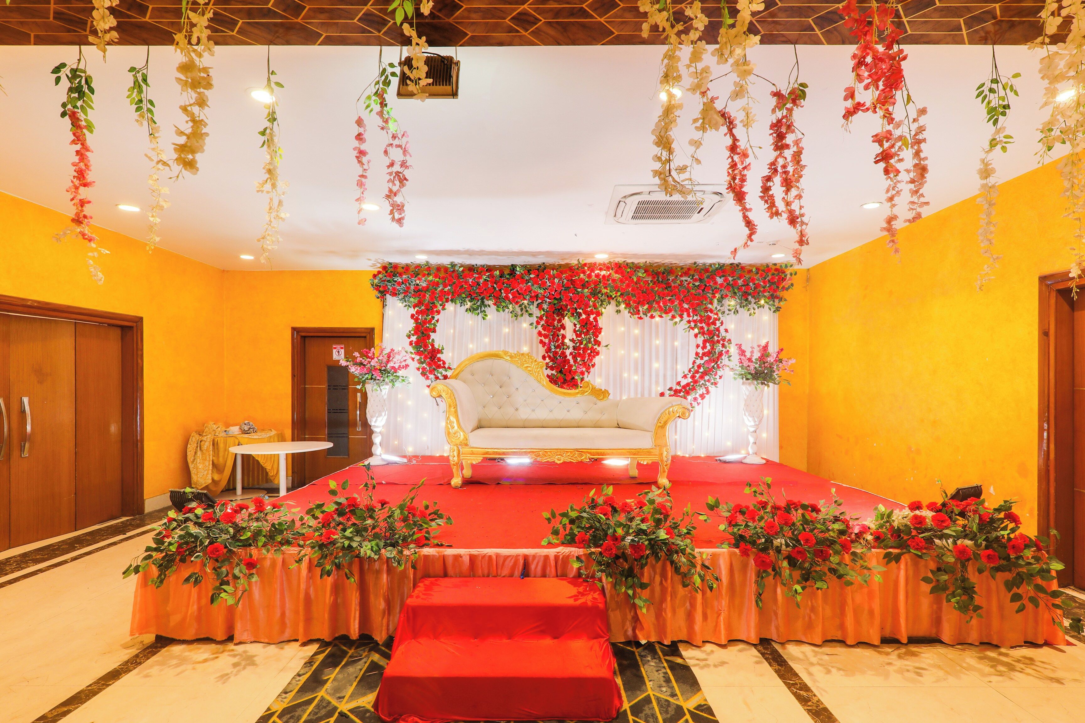 A stage with a golden sofa, red floral arrangements, and hanging decorations.