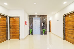 A hallway with two wooden doors, a marble wall, and a fire extinguisher. - Townhouse Oak Suchitra Kompally Road (Hyderabad)