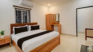 Une chambre à coucher comprenant un lit, une table de chevet, une commode, un appareil de climatisation, une fenêtre, un ventilateur de plafond et un miroir.