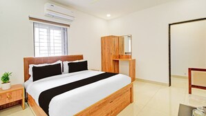 Une chambre d’hôtel comprenant un lit, une table de chevet, une plante en pot, une fenêtre, un climatiseur, un ventilateur de plafond et une armoire en bois.