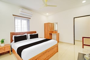 Habitación de hotel con cama, mesita de noche, planta en maceta, ventana, equipo de aire acondicionado, ventilador de techo y armario de madera.