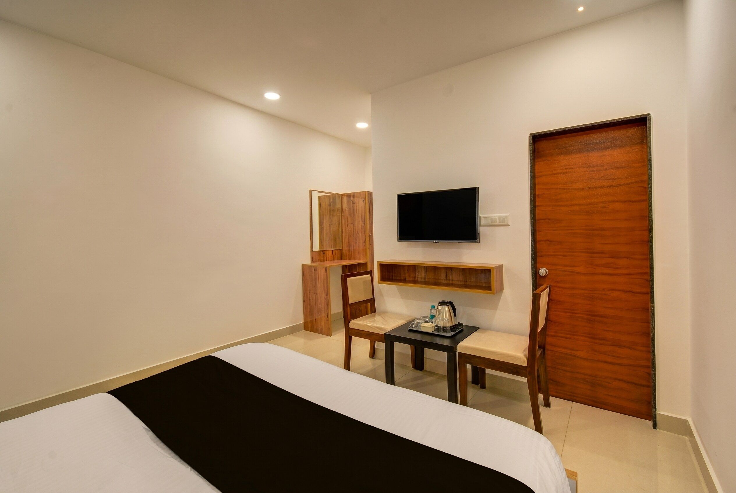 Une chambre d’hôtel avec un lit, un téléviseur fixé au mur, une porte en bois et une petite table avec une chaise.