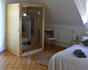 A bedroom with a wooden wardrobe, a chair, a small table with a bottle, and a bed with a blanket. - Dreamy Roof Terrace Eifelgluck (Pelm)