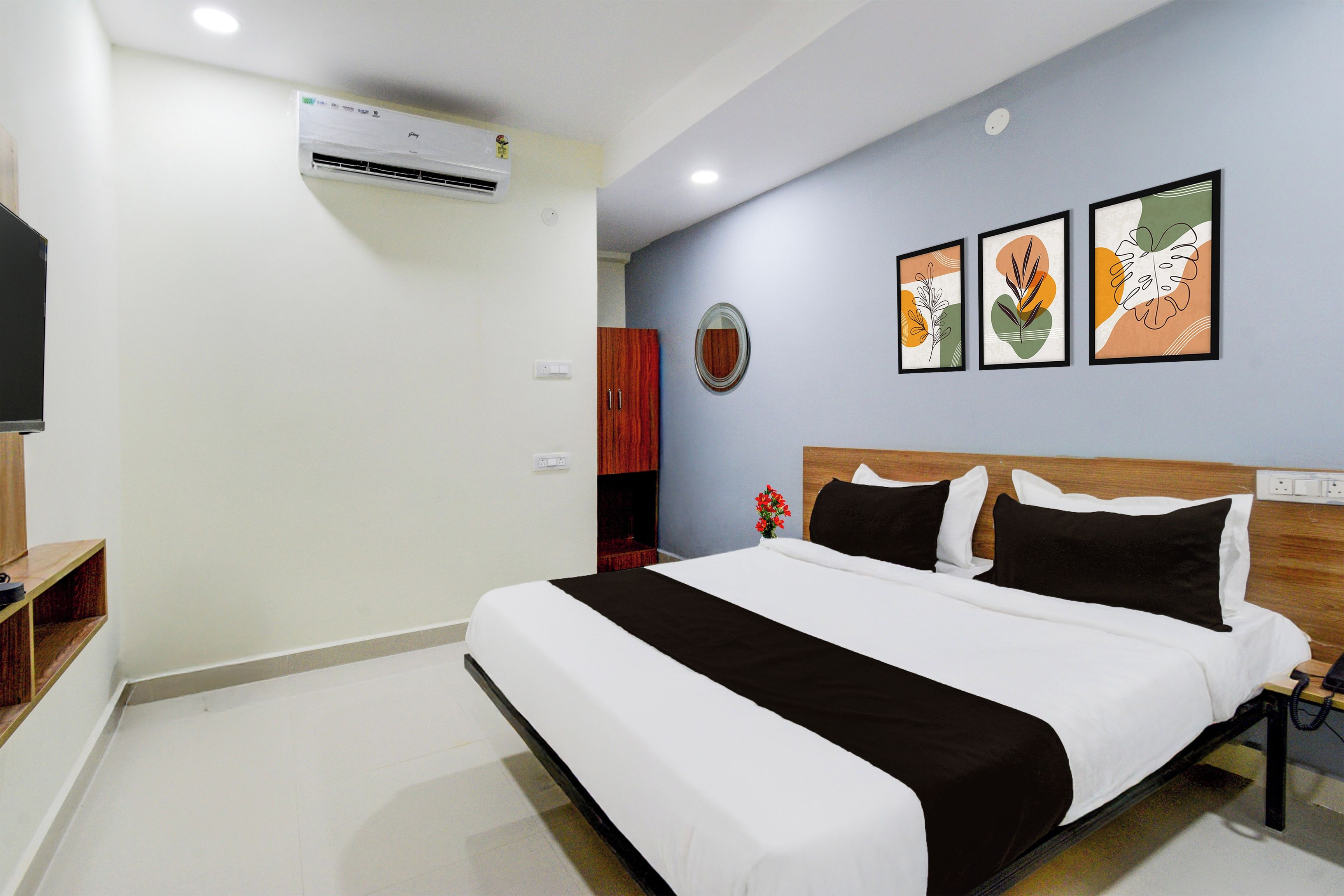 A hotel room with a large bed, a flat-screen TV, an air conditioning unit, and a wall-mounted mirror.