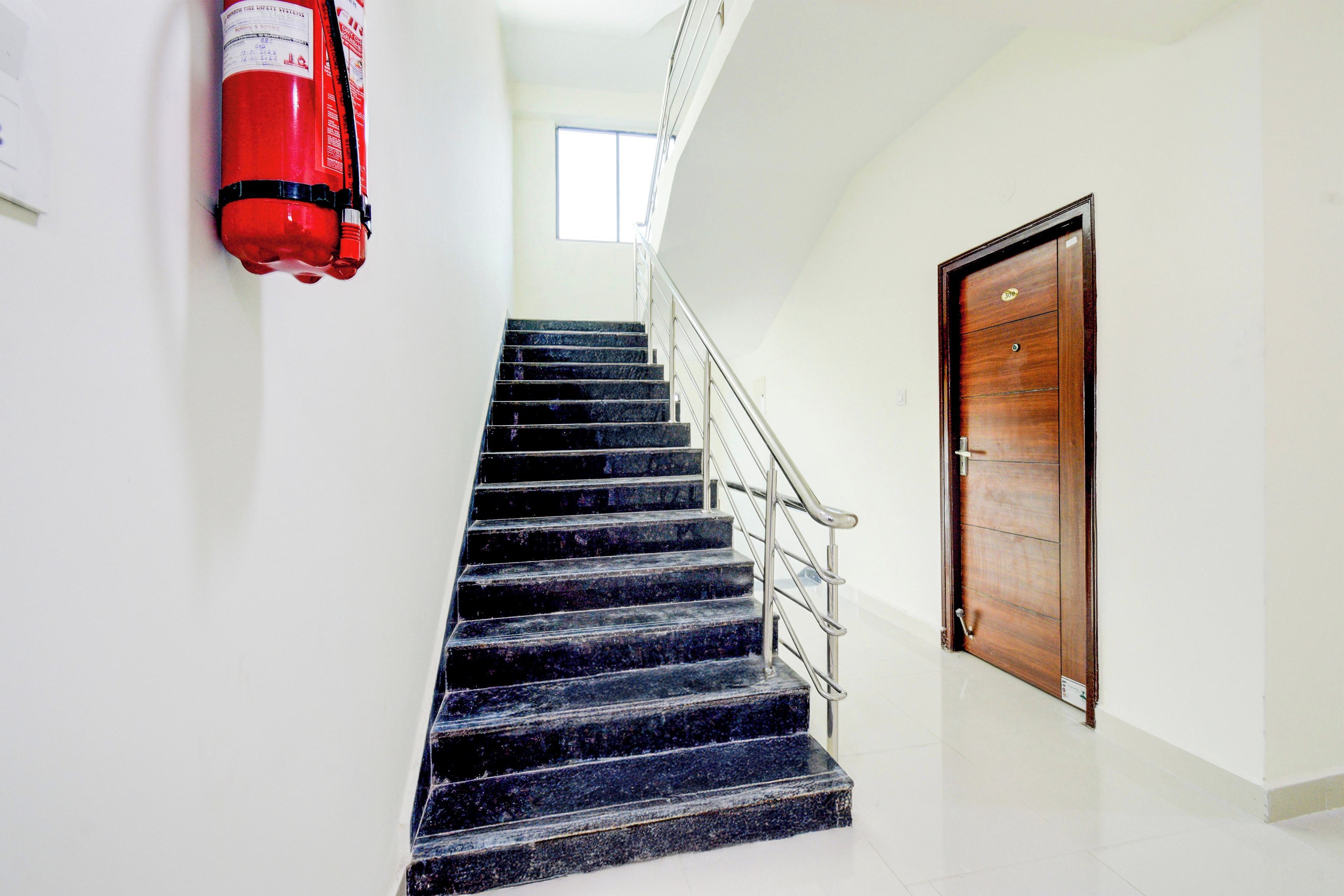 Una escalera con un extintor montado en la pared, una puerta de madera y un ventanal en la parte superior.