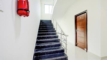 Una escalera con un extintor montado en la pared, una puerta de madera y un ventanal en la parte superior.