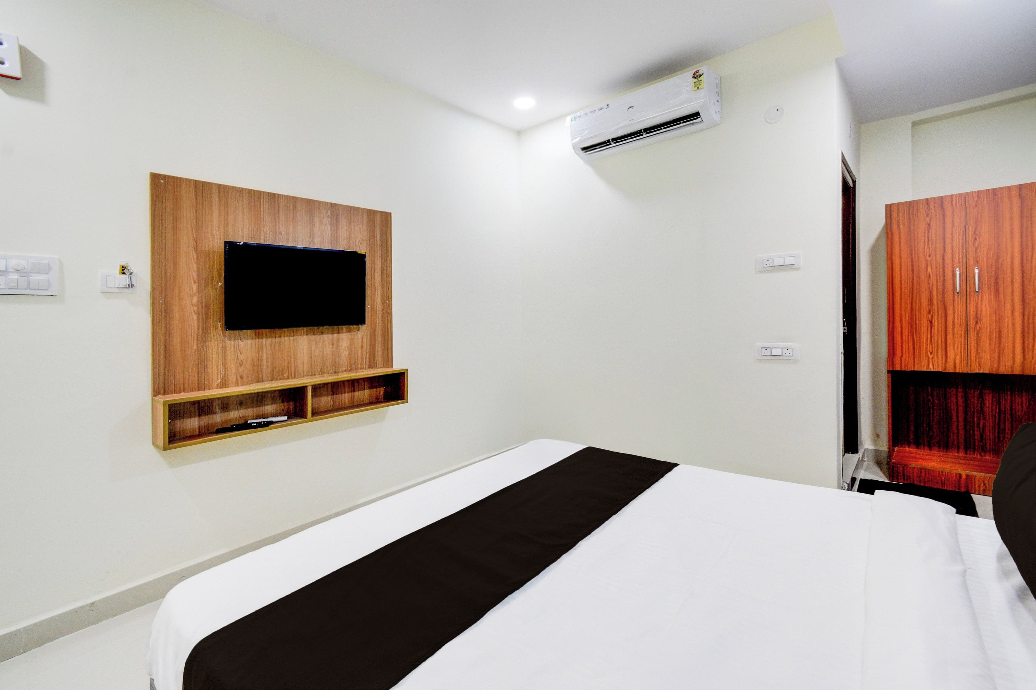 Una habitación de hotel con cama, televisión montada, aire acondicionado y armario.