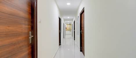Un pasillo con puertas de madera a un lado y paredes blancas al otro, que conduce a una habitación con una ventana.