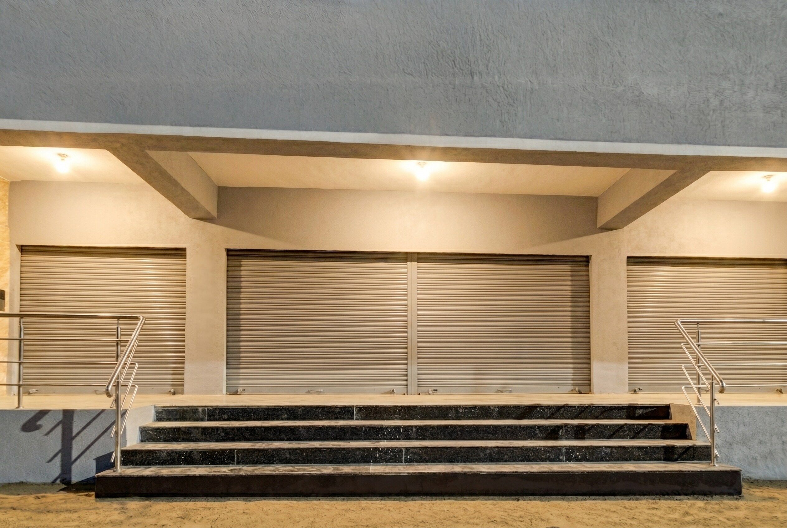A set of outdoor stairs leading to a building with closed roller shutters.