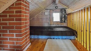 Un dormitorio tipo loft con techo inclinado, chimenea de ladrillo, ventana con cortinas y piso de madera.