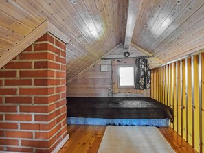 Un dormitorio tipo loft con techo inclinado, chimenea de ladrillo, ventana con cortinas y piso de madera.